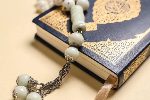 Koran with prayer beads for Ramadan on color background, closeup