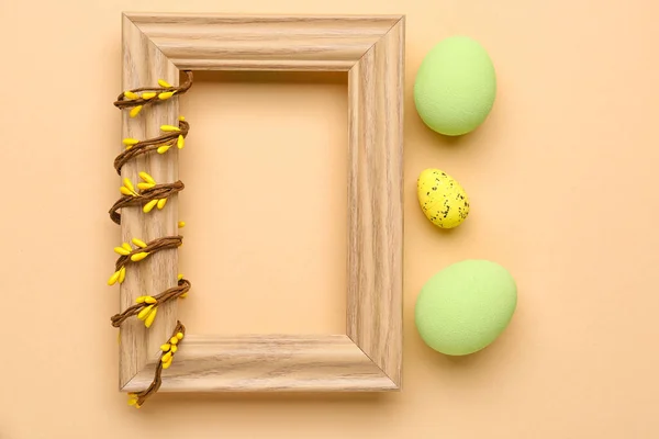 Blank wooden frame with vine and painted Easter eggs on beige background