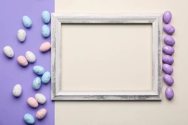 Blank wooden frame with painted Easter eggs on white and lilac background