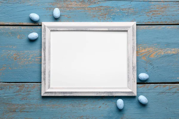 Blank frame with Easter eggs on blue wooden background