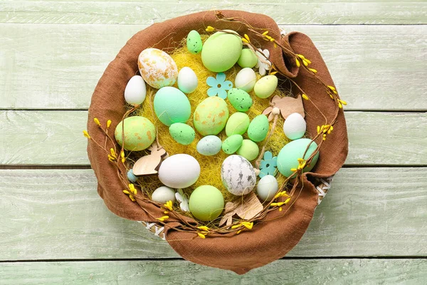 Basket with beautiful Easter eggs and decor on color wooden background