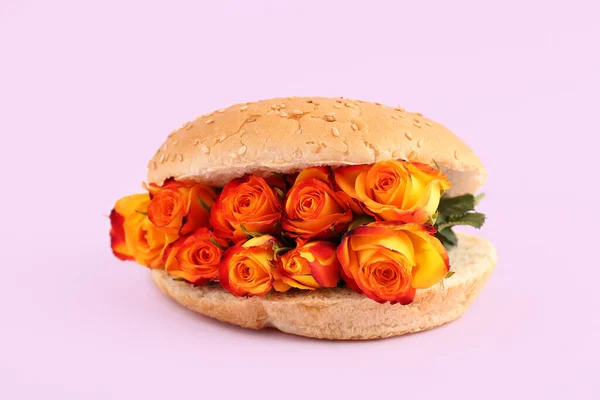 Burger bun with beautiful rose flowers on pink background