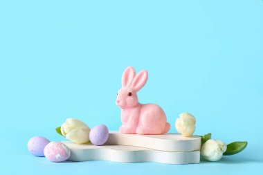 Podiums with Easter eggs and rabbit on blue background
