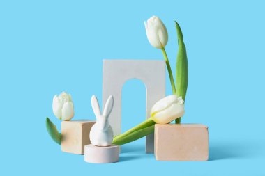 Podiums with Easter rabbit and tulips on blue background