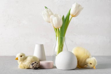 Podiums, cute chickens, Easter egg and vase with tulips on light background