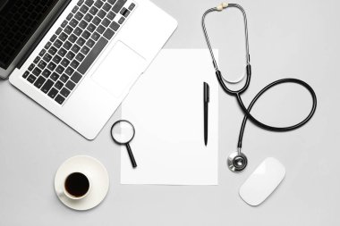 Blank paper with magnifier, stethoscope, cup of coffee and laptop on grey background. World Health Day