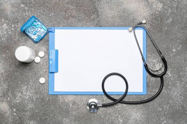 Blank clipboard with stethoscope and pills on dark background. World Health Day