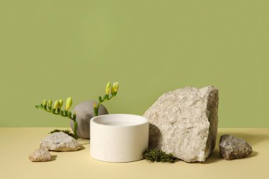 Plaster podium, stones and freesia flowers on green background