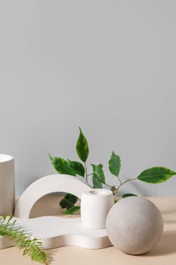 Plaster podiums with fern and ficus branches on beige table against grey background