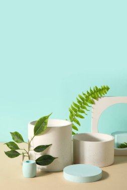Plaster podiums with ficus and fern branches on beige table against turquoise background