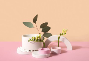 Plaster podiums with freesia flowers and eucalyptus branches on pink table against beige background