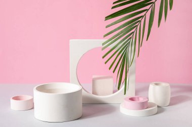 Plaster podiums and palm leaves on white table against pink background
