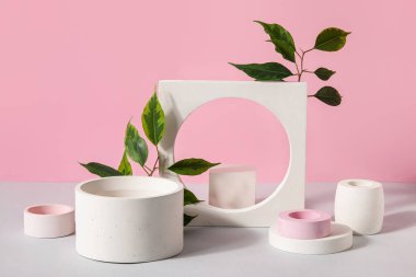 Plaster podiums and ficus branches on white table against pink background