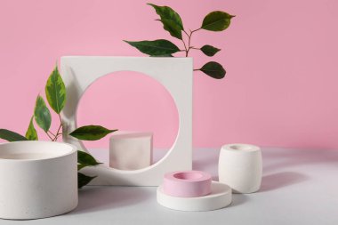 Plaster podiums and ficus branches on white table against pink background