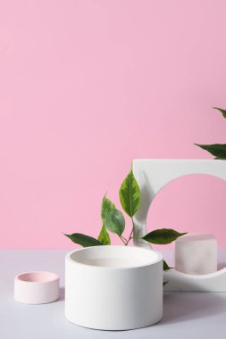 Plaster podiums and ficus branches on white table against pink background