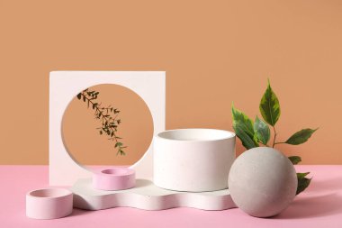 Plaster podiums with ficus and eucalyptus branches on pink table against brown background