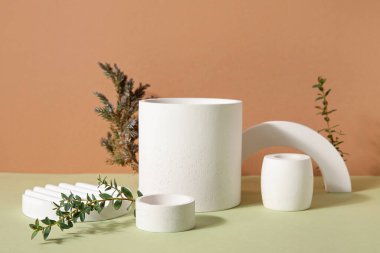 Plaster podiums with eucalyptus and spruce branches on green table against brown background