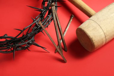 Crown of thorns with nails and mallet on red background