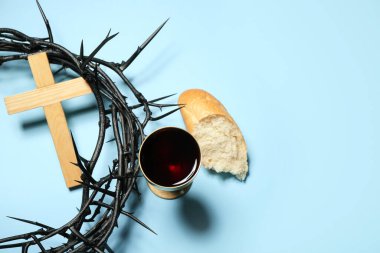 Crown of thorns, cross, cup of wine and bread on blue background