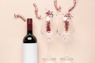 Composition with bottle of wine, glasses, serpentine and sequins on beige background