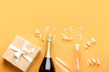 Bottle of champagne, gift box, glasses and  serpentine on orange background