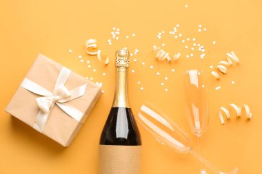 Bottle of champagne, gift box, glasses and  serpentine on orange background
