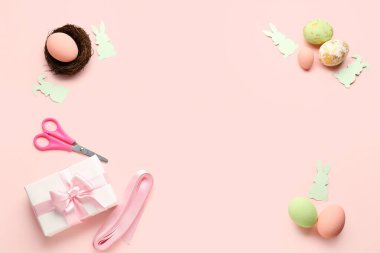 Frame made of Easter eggs, gift and paper rabbits on pink background