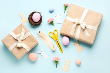 Gifts with Easter eggs, paper rabbits, flowers and materials on blue background