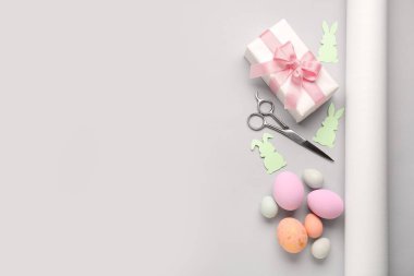 Gift with Easter eggs, scissors and paper rabbits on grey background