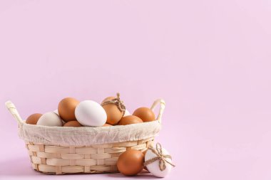 Wicker basket with Easter eggs on lilac background