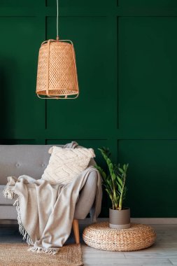 Grey sofa with cushion, plaid and houseplant on pouf near green wall in living room