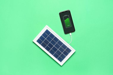 Portable solar panel charging mobile phone on green background