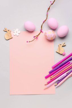 Blank paper sheet with rabbits, tree branch, pens and Easter eggs on grey background