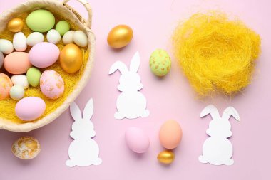 Paper rabbits and basket with Easter eggs on pink background