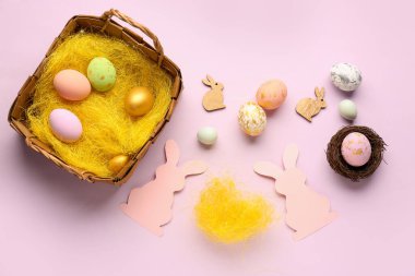 Paper rabbits and basket with Easter eggs on pink background
