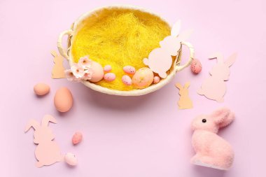 Frame made of basket with Easter eggs and paper rabbits on pink background