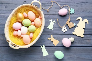 Basket with Easter eggs and paper rabbits on dark wooden background