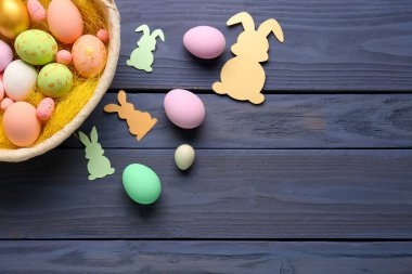 Basket with Easter eggs and paper rabbits on dark wooden background