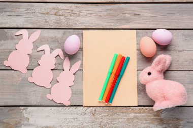 Blank card with pens, Easter eggs and rabbits on wooden background