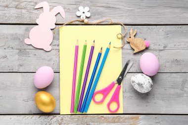 Blank card with pencils, scissors, Easter eggs and rabbits on wooden background