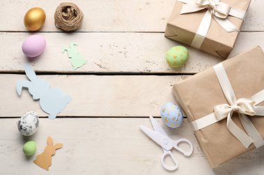 Frame made of gifts, Easter eggs, scissors and rope on white wooden background
