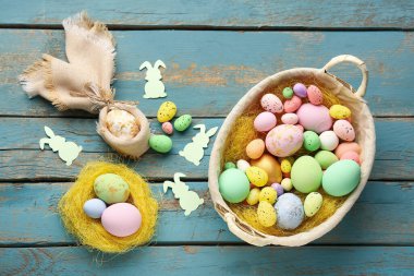 Basket with Easter eggs and paper rabbits on blue wooden background