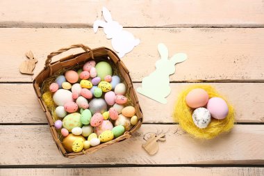 Basket with Easter eggs and paper rabbits on beige wooden background