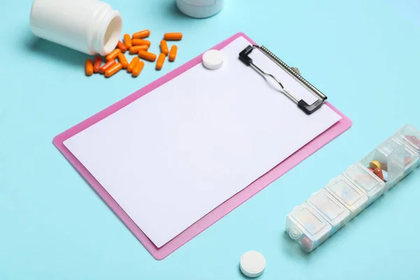 Blank clipboard with pills on blue background, closeup. World Health Day