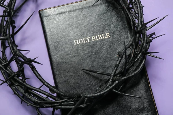 Crown of thorns and Holy Bible on lilac background, closeup