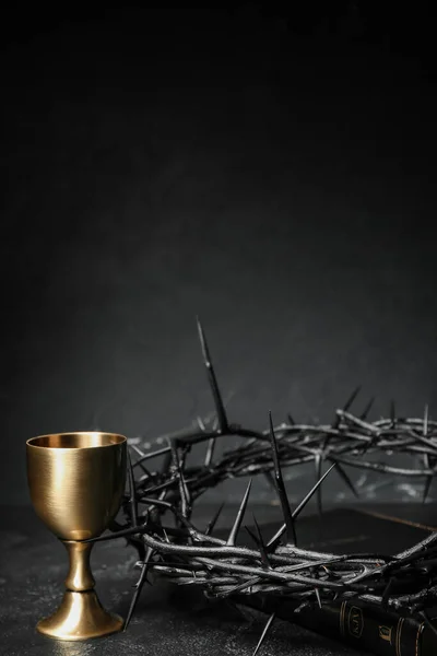 Crown of thorns with Holy Bible and cup of wine on dark background