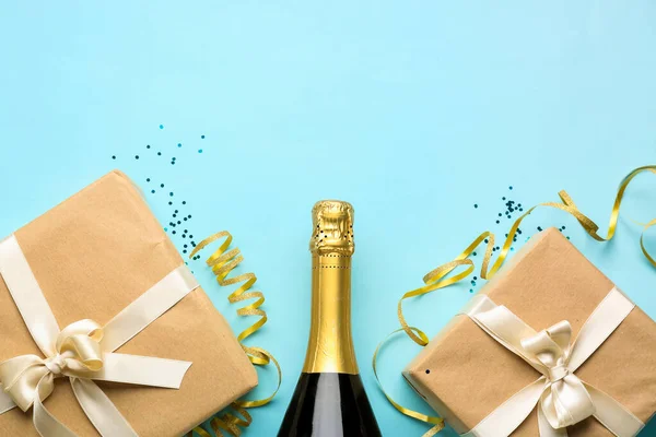 Bottle of champagne, gift boxes, serpentine and sequins on blue background