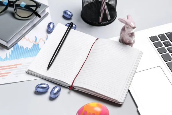 Blank notebook with office stationery, laptop and Easter eggs on grey background