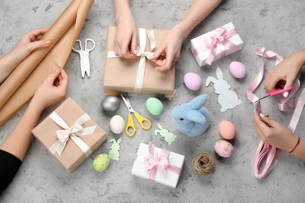 Women wrapping Easter gifts on grunge background, top view