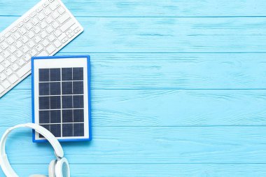 Composition with portable solar panel, keyboard and wireless earphones on blue wooden background